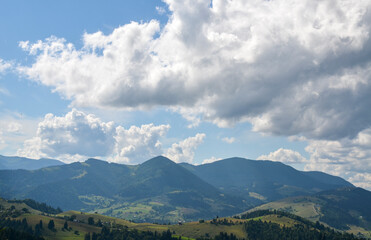 Fototapeta premium Picturesque mountain landscape with green meadows and rural houses located on the hills. Green forests cover the mountains and slopes in the background. Carpathians, Ukraine