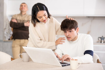 Girl persuades a young guy to stop playing computer games. Upset father in the background