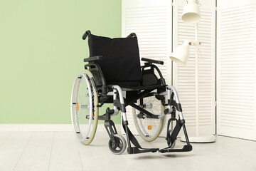 Modern empty wheelchair with folding screen and lamp near green wall