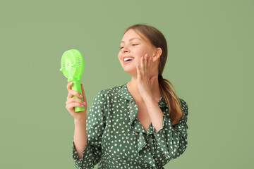Beautiful young woman with handheld mini fan on green background