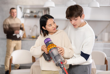 Young guy and young woman using vacuum cleaner to clean floor in kitchen at home