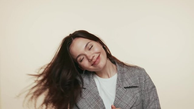 A young woman with brunette hair lets loose, dancing in a fashionable plaid coat with a beaming smile and positive energy in slow motion.