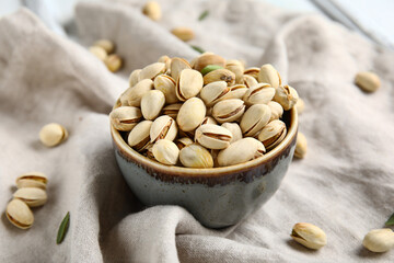 Bowl with tasty pistachio nuts on napkin