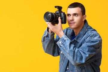 Male photographer with modern camera on yellow background