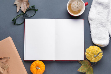Composition with blank open book, socks, cup of coffee and autumn decor on dark background