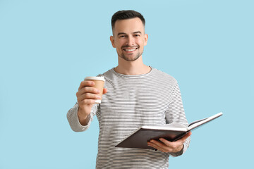 Happy young man with book and cup of coffee on blue background