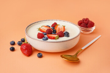 Bowl of tasty semolina porridge with fresh berries on orange background