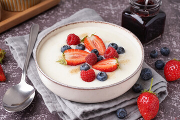 Bowl of tasty semolina porridge with fresh berries on grey background