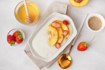 Bowl of tasty semolina porridge with nectarine, berries and honey on white background