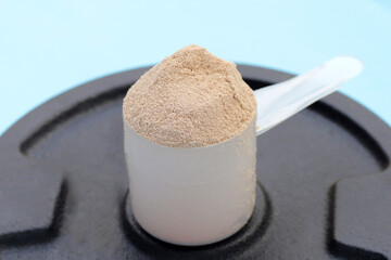 Whey protein powder with iron weight plates on blue background.