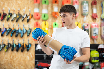 Young guy carefully selects climbing rope for a hike in a sports equipment store