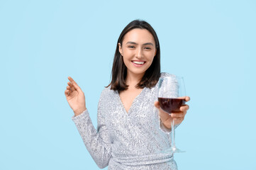 Beautiful young woman with glass of red wine on blue background