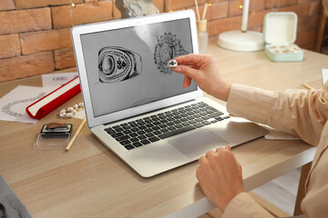 Female jeweler with ring and sketch on laptop in workshop, closeup