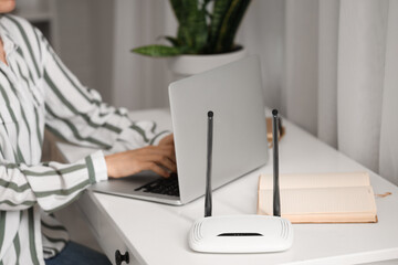 Modern wi-fi router on table of working woman with laptop, closeup