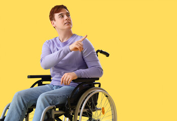 Young man in wheelchair pointing at something on yellow background