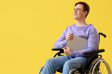 Young man in wheelchair with laptop on yellow background