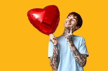 Handsome young man with heart-shaped air balloon on yellow background