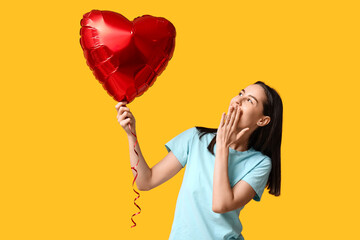 Happy young woman with heart-shaped air balloon on yellow background