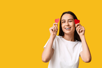 Beautiful young woman with paper hearts on yellow background