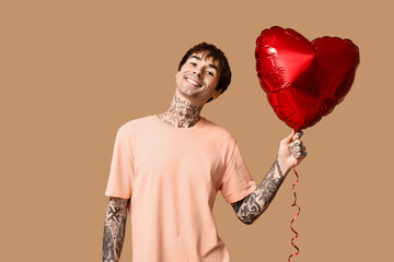 Handsome young man with heart-shaped air balloon on beige background