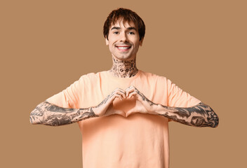 Handsome young man making heart with hands on beige background