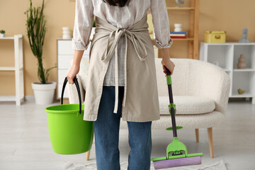 Young woman with floor mop and bucket in living room, back view