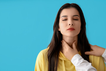 Endocrinologist examining thyroid gland of young woman on blue background