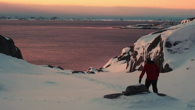 Person walking in extreme cold arctic sunset during the winter with the ocean in the background - Greenland, Nuuk