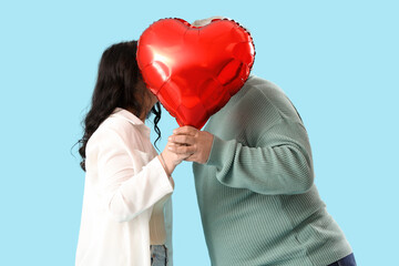 Beautiful mature couple with heart-shaped balloon on blue background. Valentine's Day celebration