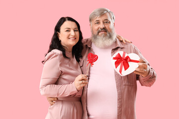 Beautiful mature couple with gift box and heart on pink background. Valentine's Day celebration