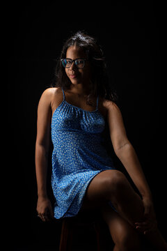 Young woman with straight hair wearing glasses and a blue dress posing for a photo.