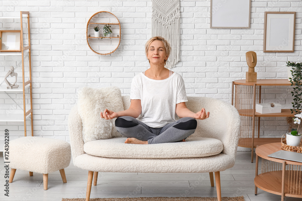 Canvas Prints mature woman meditating while sitting on couch at home