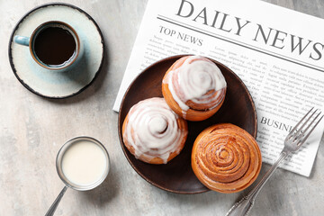 Cinnamon buns with cream, cup of coffee and newspaper on grey grunge background