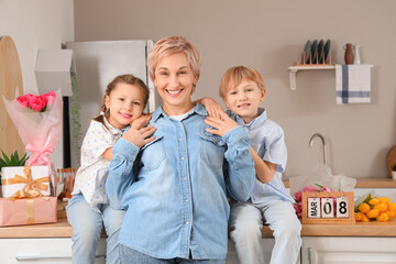 Little children and their grandmother hugging in kitchen. International Women's Day
