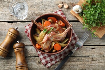 Tasty cooked rabbit with vegetables served on wooden table, flat lay
