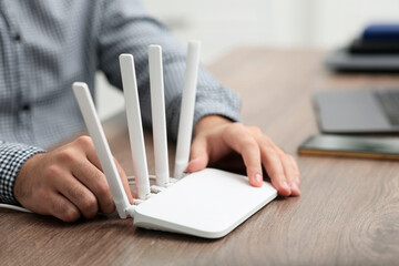 Man inserting cable into Wi-Fi router at wooden table indoors, closeup