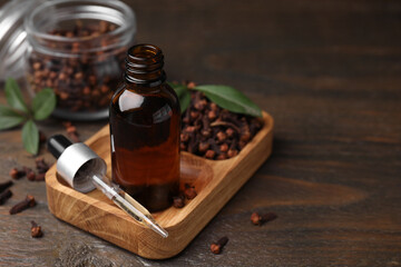 Clove oil in bottle, pipette and dried buds on wooden table, closeup. Space for text