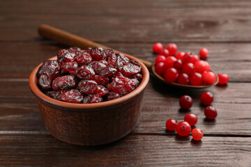 Tasty dried cranberries in bowl and fresh ones on wooden table, closeup