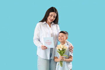 Beautiful woman and her little son holding greeting card and bouquet of tulips on blue background. International Women's Day