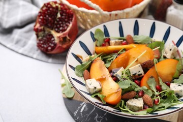 Tasty salad with persimmon, blue cheese, pomegranate and almonds served on white table, closeup. Space for text