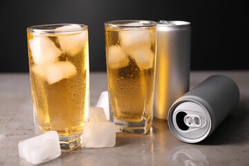 Tasty energy drink with ice cubes in glasses and aluminium cans on grey table, closeup