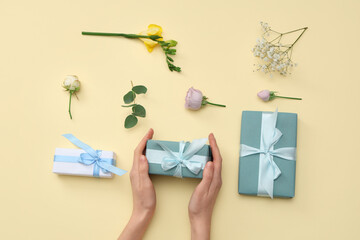 Female hands with gift boxes and beautiful flowers on yellow background. International Women's Day