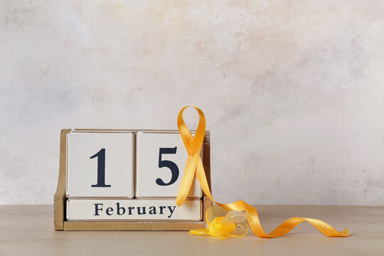 Calendar with golden ribbon and pacifier on wooden table against white grunge background. Childhood cancer awareness concept