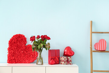 White cabinet with heart, bouquet of roses and gift boxes near blue wall. Valentine's Day...