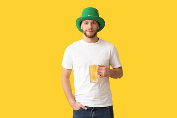 Young man in leprechaun hat with glass of beer on yellow background. St. Patrick's Day celebration