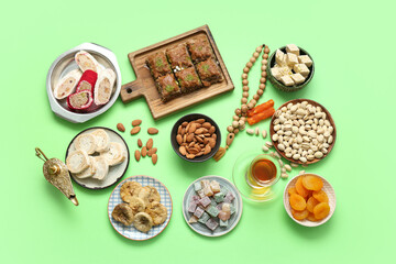 Composition with different Eastern sweets, Aladdin lamp and tasbih for Ramadan on green background