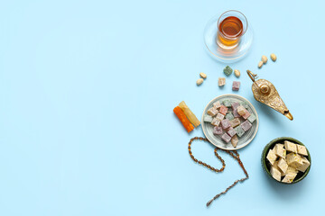 Composition with traditional Eastern sweets, tea, tasbih and Aladdin lamp for Ramadan on color background