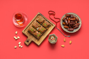 Composition with tasty Eastern sweets, tasbih and Muslim lantern for Ramadan on red background