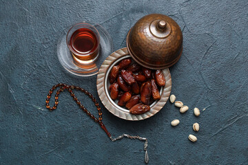 Bowl with dried dates, tea and tasbih for Ramadan on dark color background