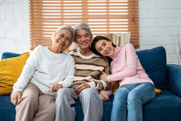 Portrait of Asian senior couple sitting on sofa with daughter in house. 